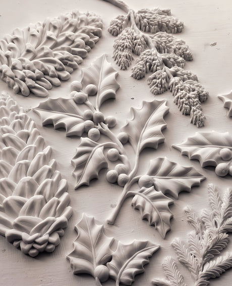Pinecones and holly leaves crafted using I.O.D. Winter Forage Mould (2025 Limited Release) on white textured surface.