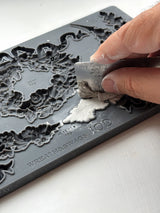Hand pressing clay into IOD Wreath & Swags Mould with a ruler on a white surface.