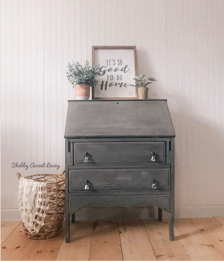 Gray desk with drawers in Zinc by Old Fashioned Milk Paint, decorated with potted plants and a framed sign on top.