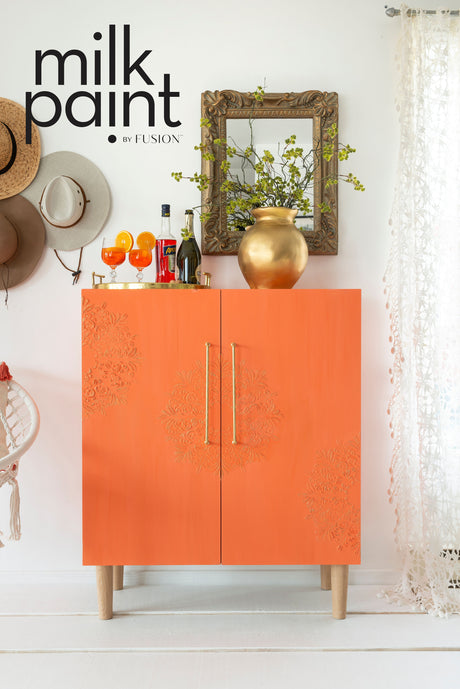 Orange cabinet painted in Aperol Spritz Milk Paint by Fusion Mineral Paint, shown near drinks and a mirror.