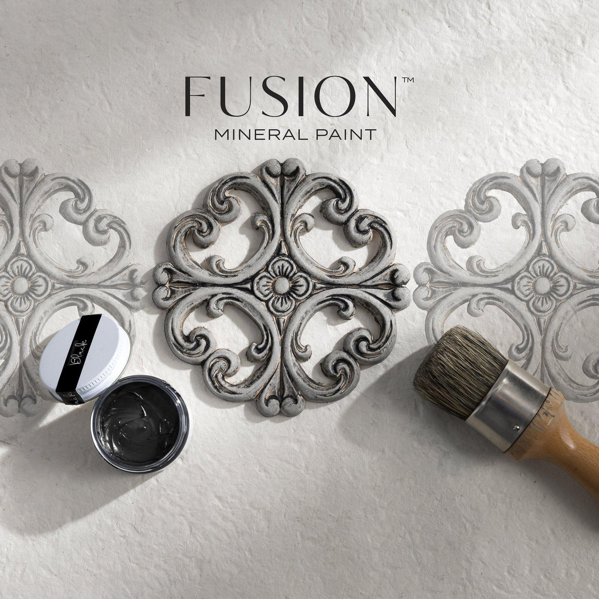 Round stencil, paintbrush, and Fusion Mineral Paint Black Furniture Wax with two stenciled designs on white surface.
