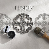 Round stencil, paintbrush, and Fusion Mineral Paint Black Furniture Wax with two stenciled designs on white surface.