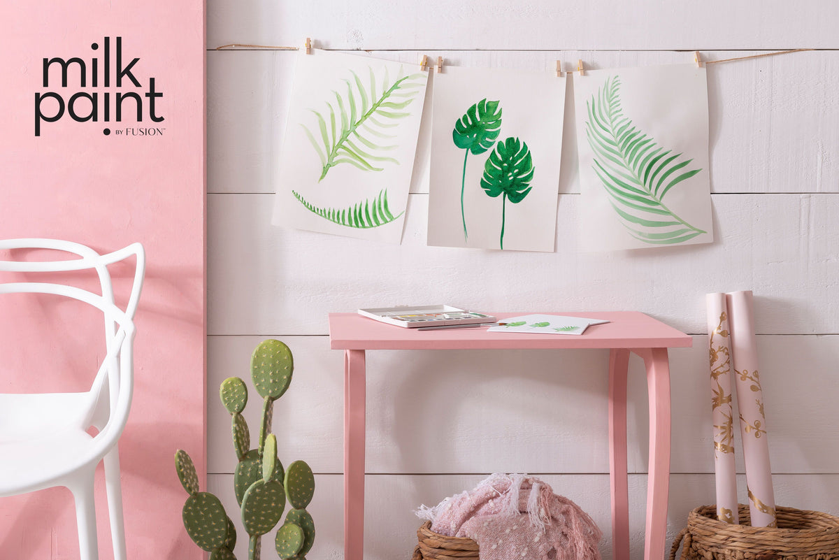 Botanical prints above a table painted in Fusion Mineral Paint Palm Springs Pink, with art supplies on the surface.