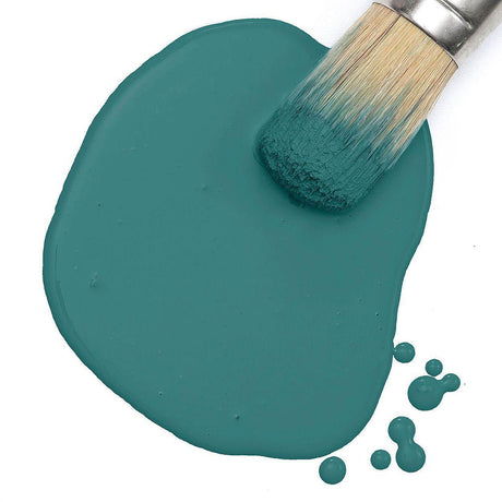 Paintbrush on a puddle of Terrarium Milk Paint by Fusion Mineral Paint, droplets visible on white surface.