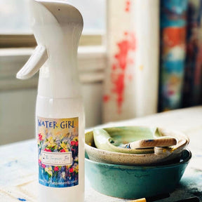 Paint Pixie Water Girl Continuous Misting Spray Bottle next to Turquoise Iris bowls and paintbrushes on a table.