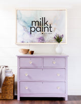 Dresser painted in Fusion Mineral Paint Wisteria Row, topped with bowls, a vase, and a milk paint sign above.