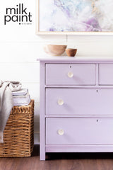 Lavender three-drawer dresser painted in Wisteria Row by Fusion Mineral Paint, with bowls on top and basket beside.